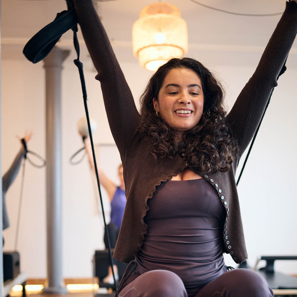 Reformer Pilates teacher poses with arms up in a classes in Yogarise Peckham