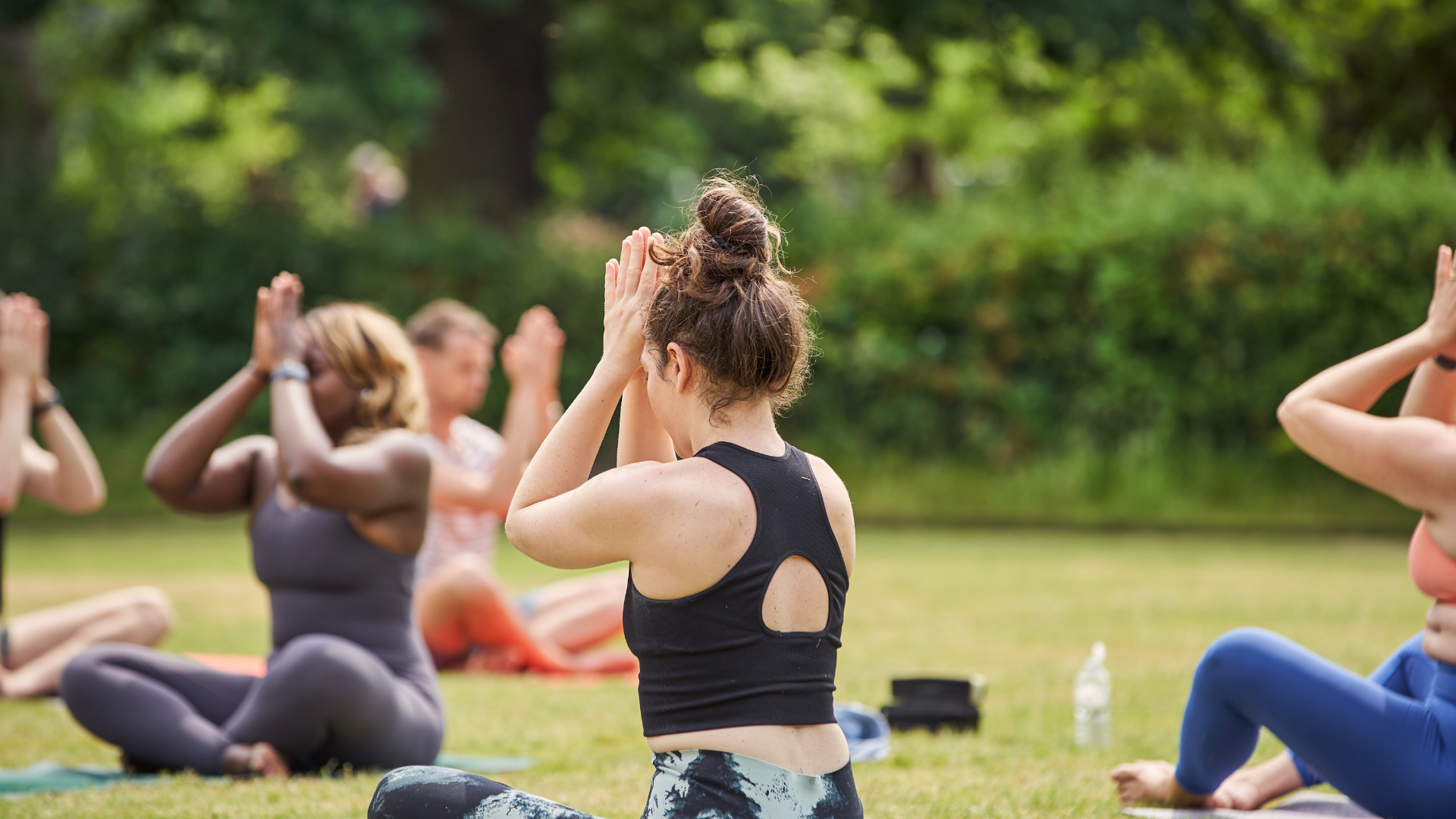 Students practicing an outdoor summer yoga class at Peckham Bowls in Peckham Rye Park, hosted by Yogarise London.